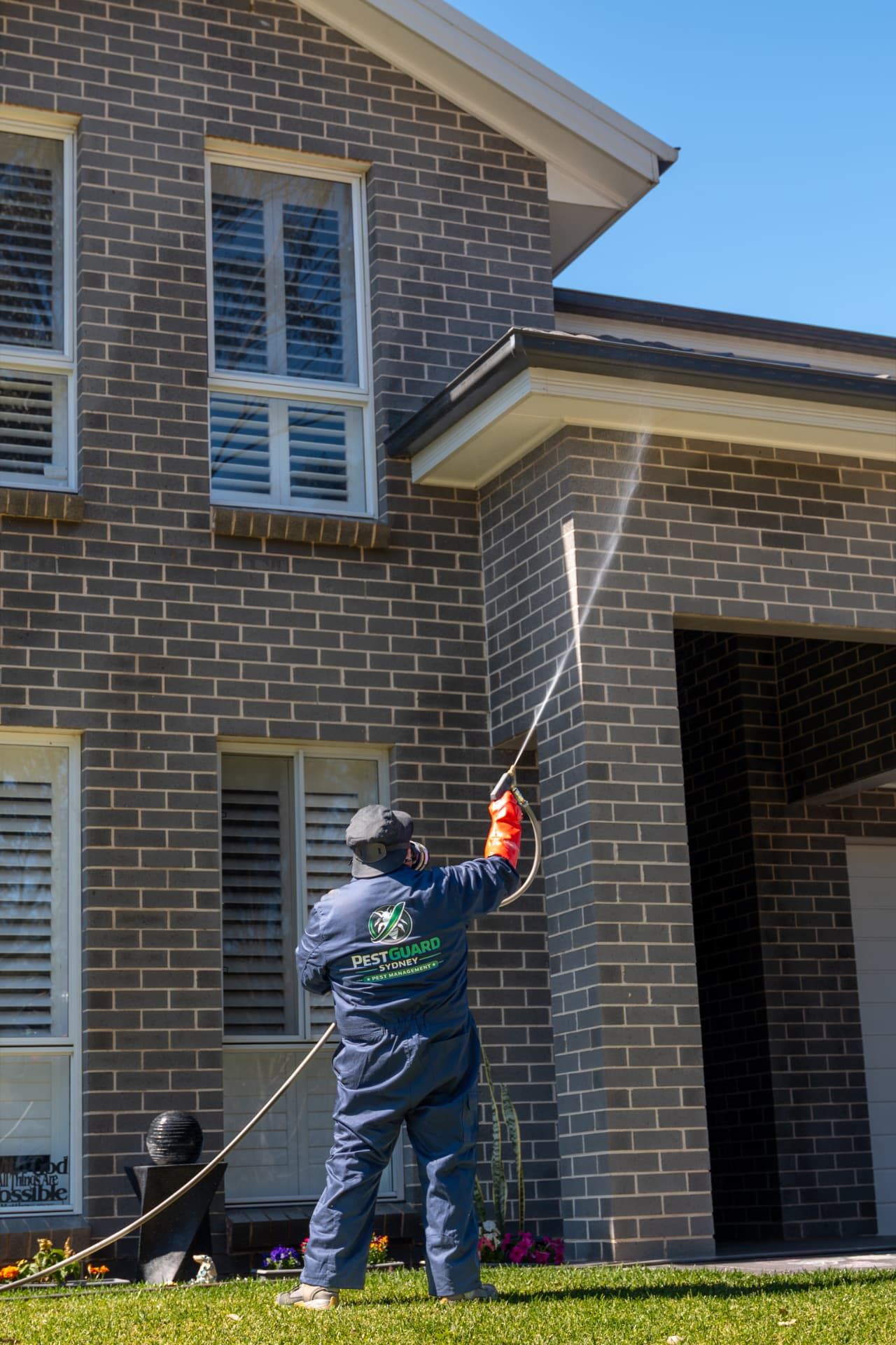 PestGuard Sydney technician spraying the eaves and gable line of a two-storey grey brick home for spiders and general pests